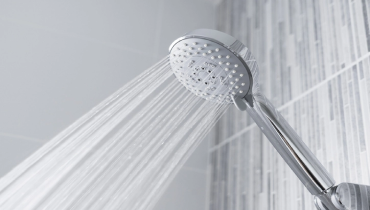 A modern handheld showerhead spraying water. It is mounted on a tiled shower wall with a sleek and clean design. | Mr. Rooter® Plumbing of Yavapai, Coconino & Maricopa Counties