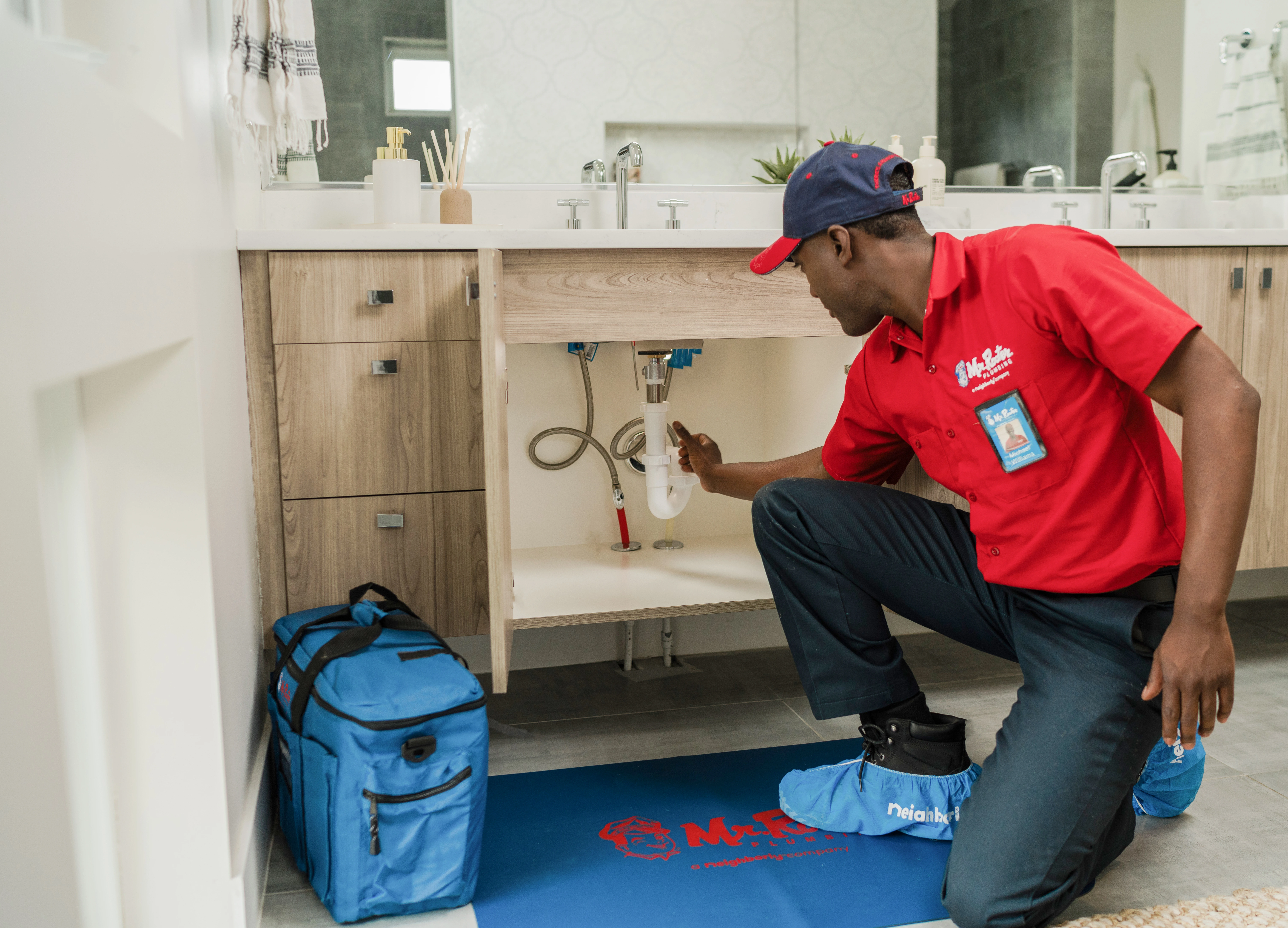 A Mr. Rooter service professional inspecting kitchen sink plumbing for leaks during annual home plumbing maintenance.