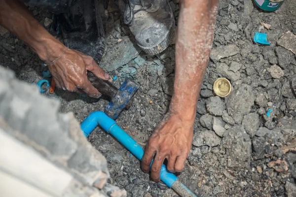 A plumber&rsquo;s hands installing a PVC pipe in a concrete floor.